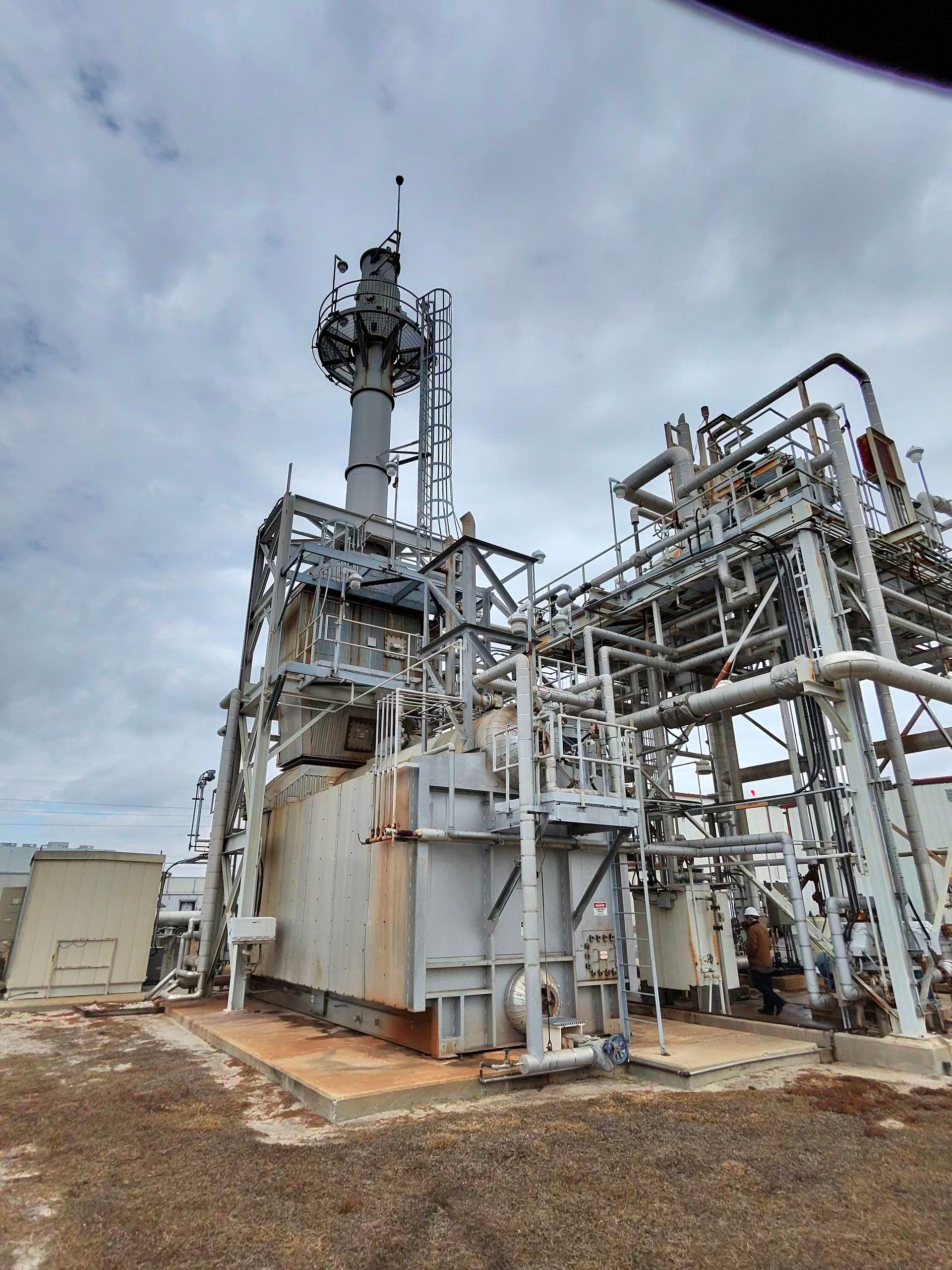 Industrial plant with tall metal towers, piping, and equipment under a cloudy sky