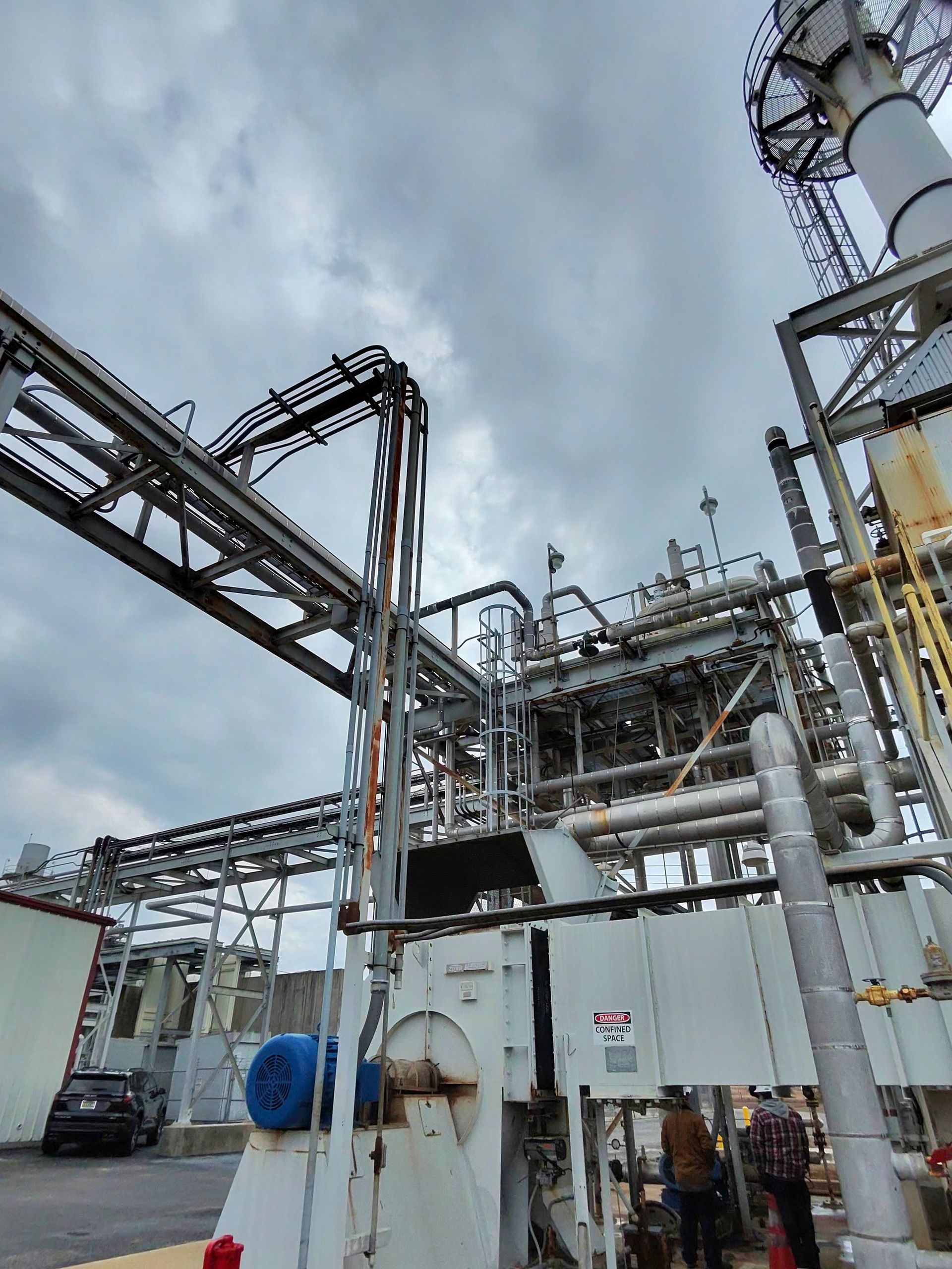 Industrial plant with metal pipes, tanks, and catwalks under a cloudy sky