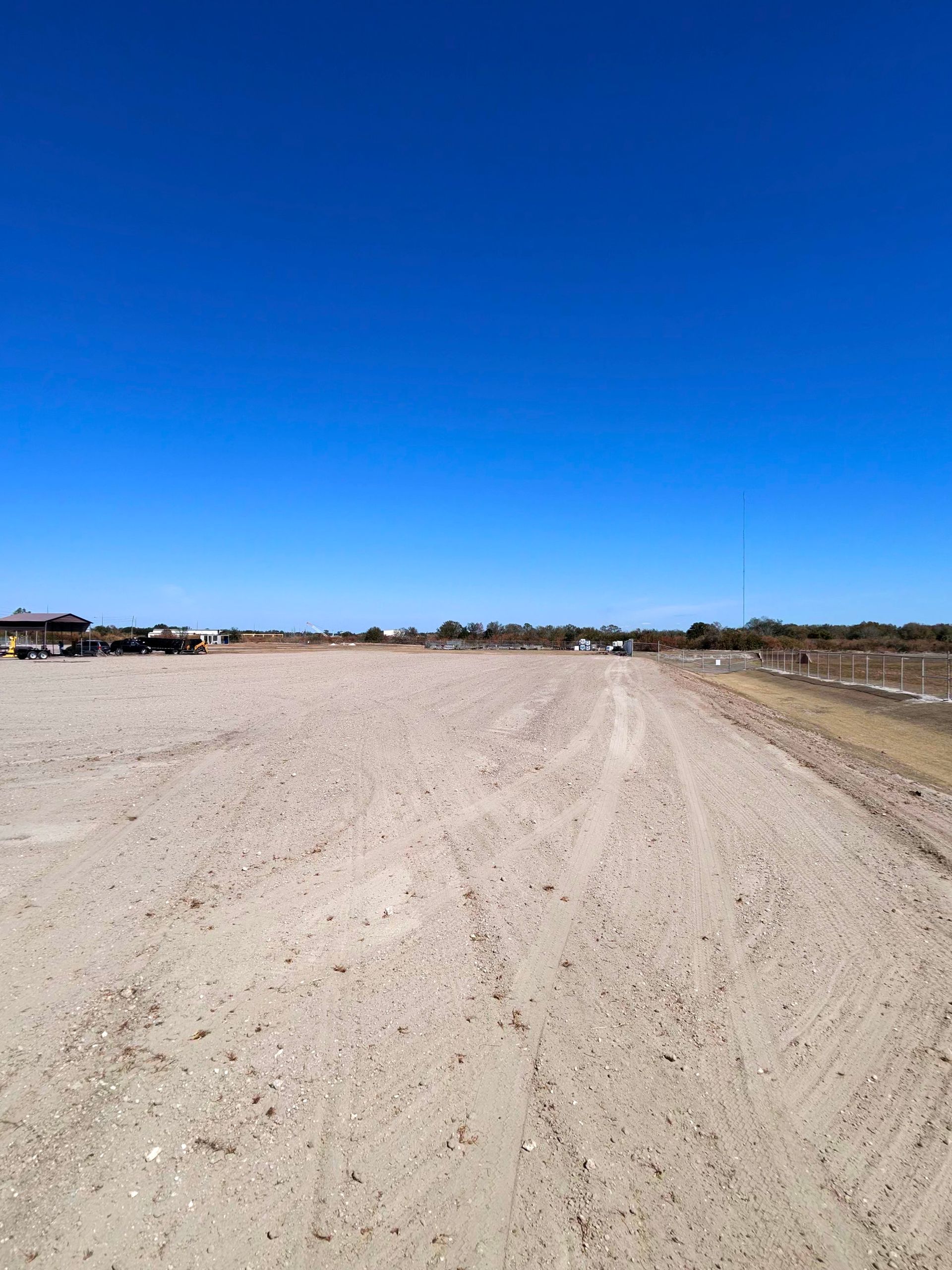 Wide sandy open field under a clear blue sky, with a dirt path curving into the distance