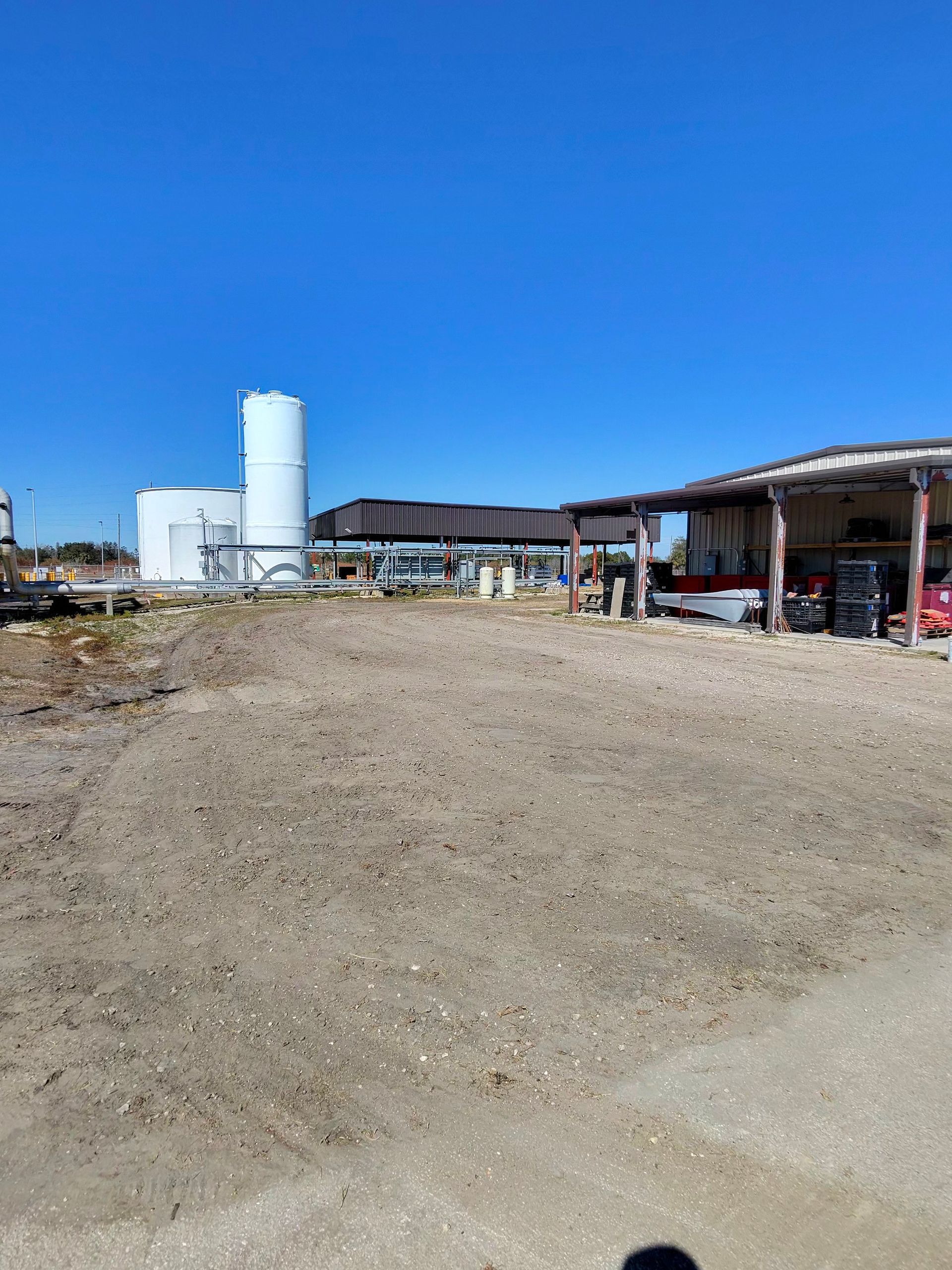 Wide dirt lot beside a farm building with a white silo under a clear blue sky