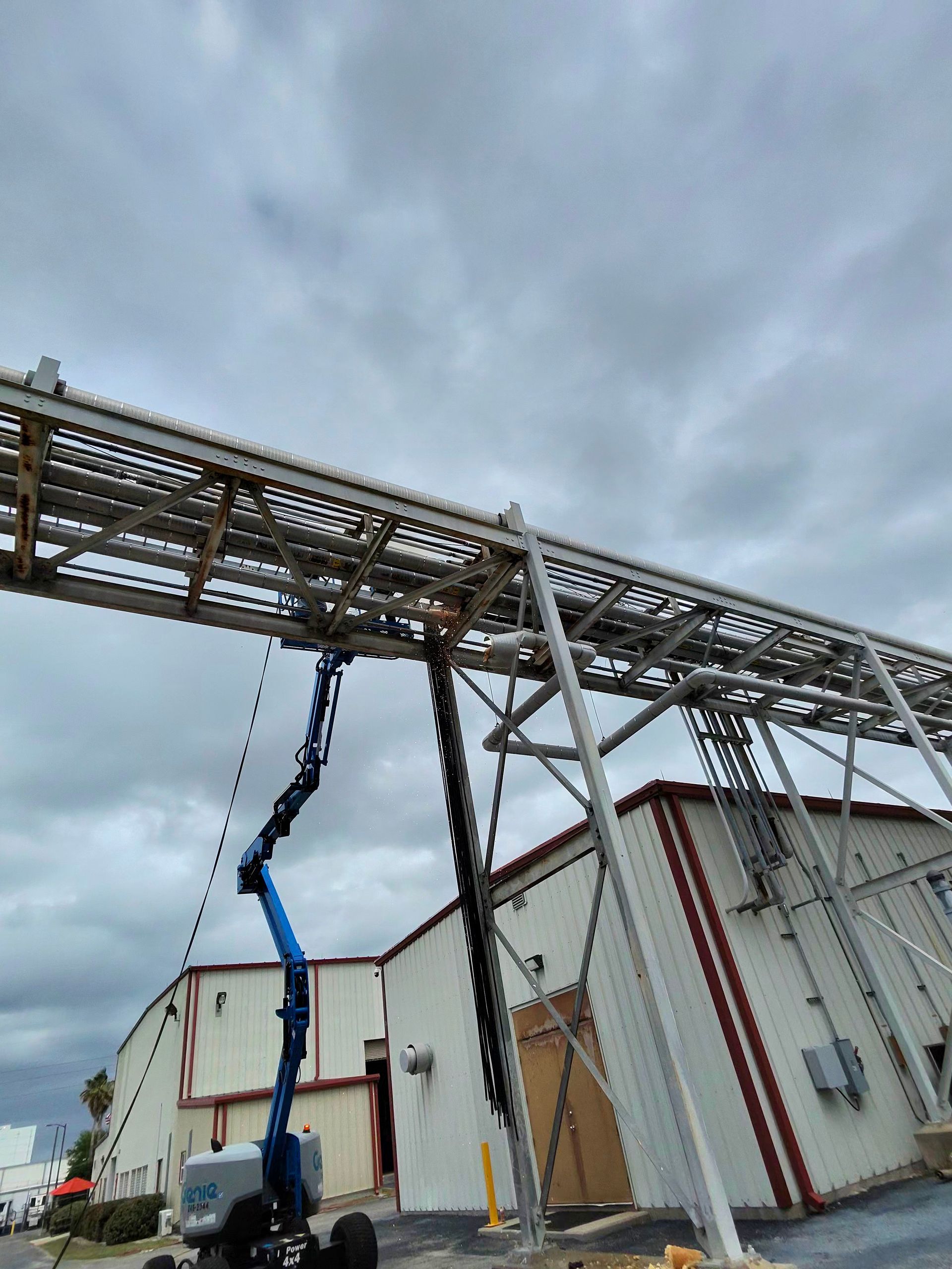Blue boom lift working beside a white industrial building under a cloudy sky
