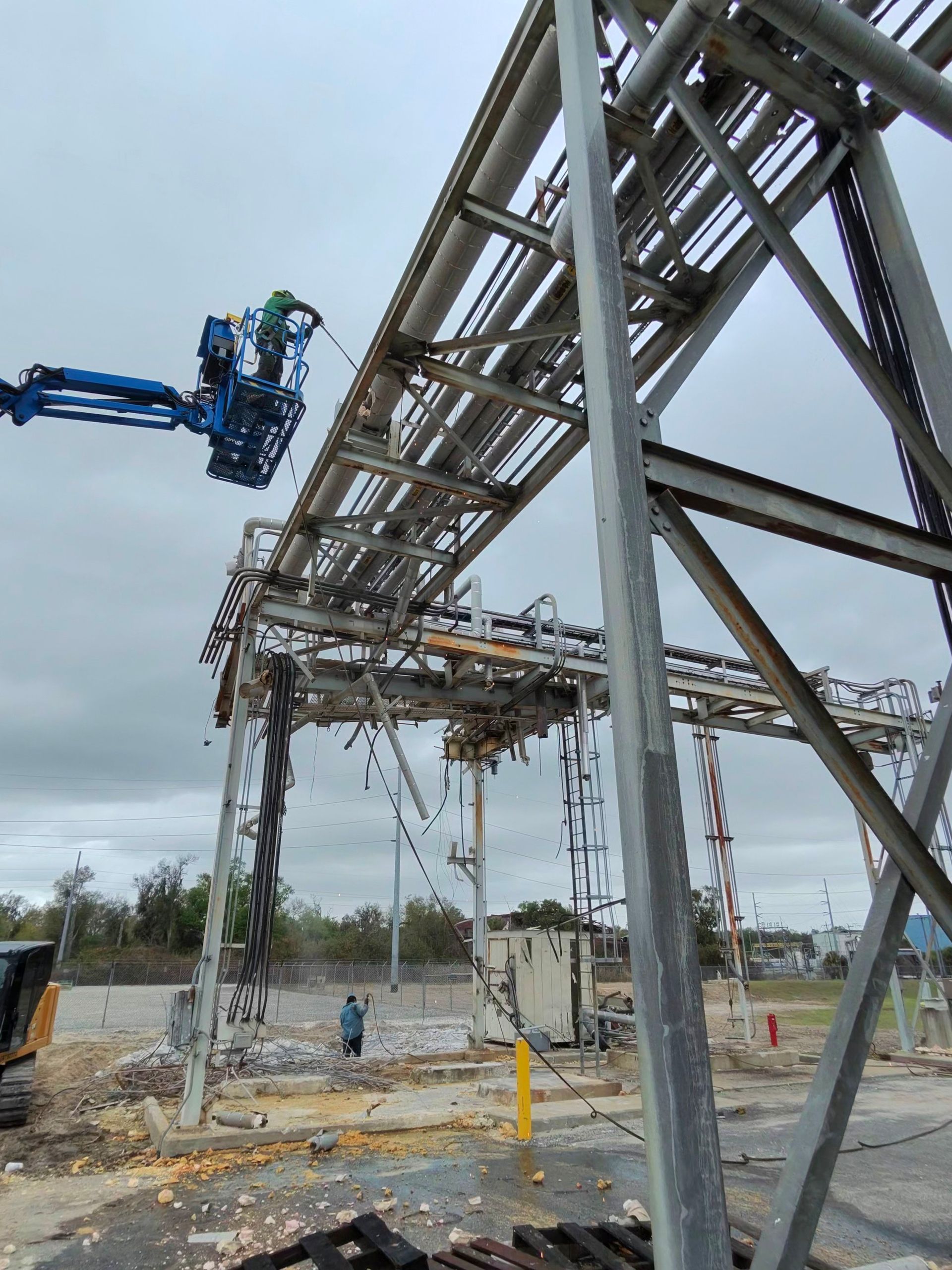 Blue boom lift working beside a large metal industrial structure at a construction site