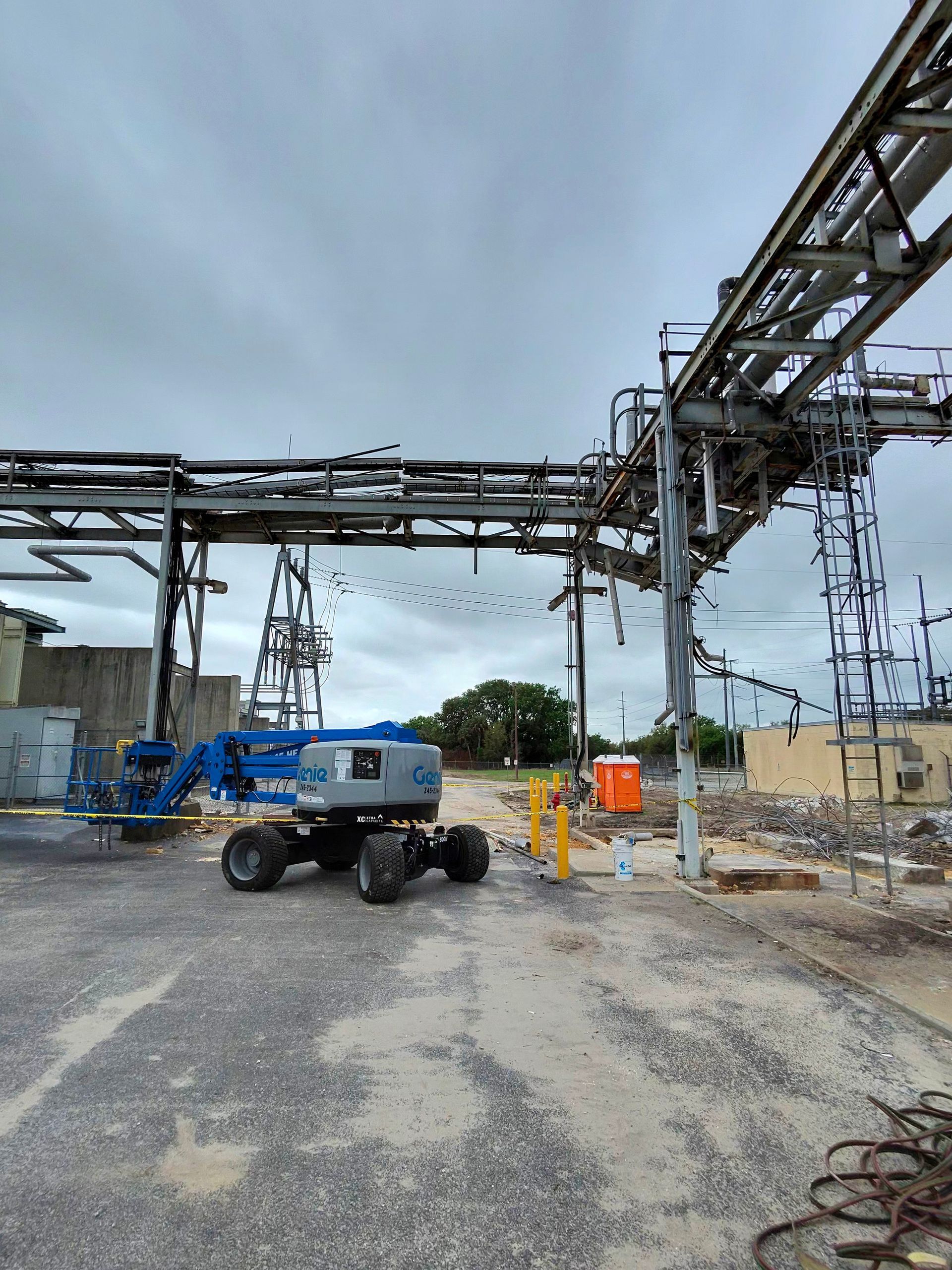Blue boom lift under metal industrial piping at a construction site