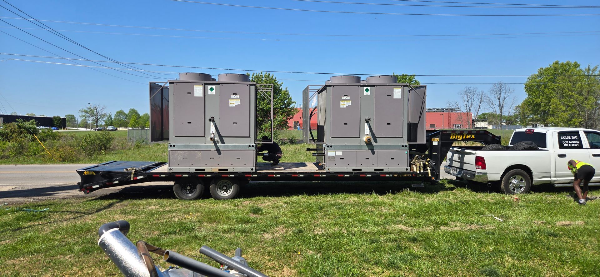 Two gray utility boxes on a trailer beside a white pickup in a grassy field