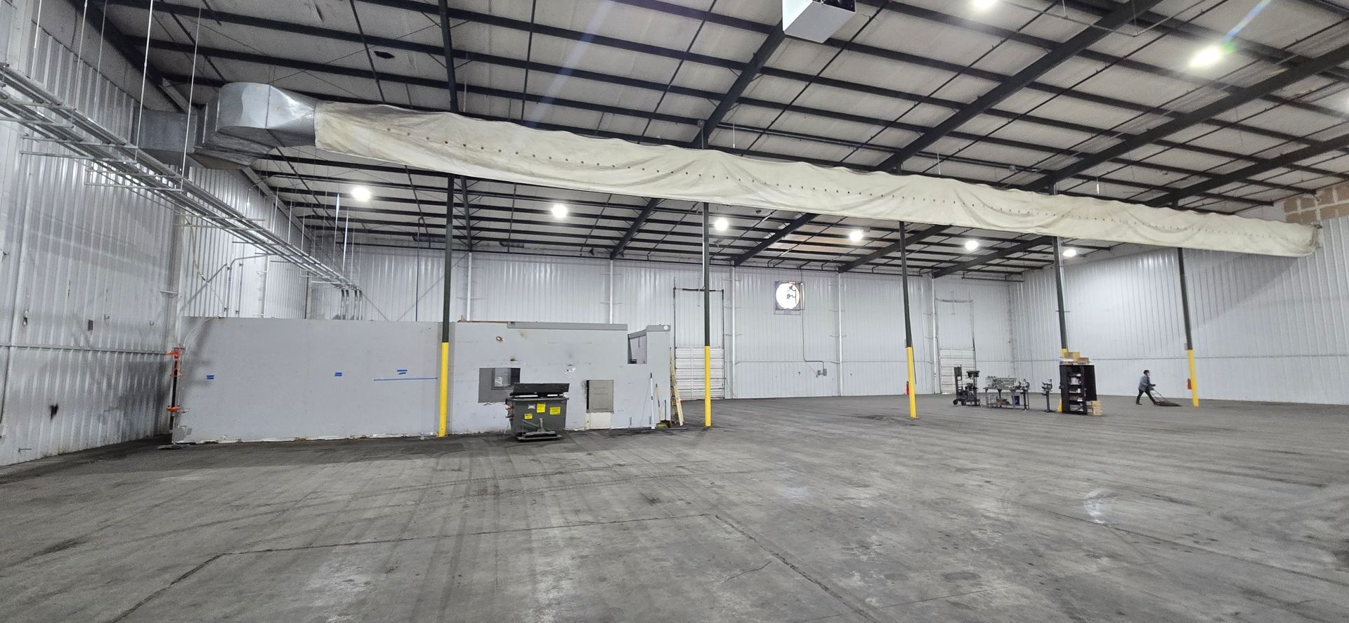 Empty industrial warehouse with high metal ceiling, white walls, and concrete floor
