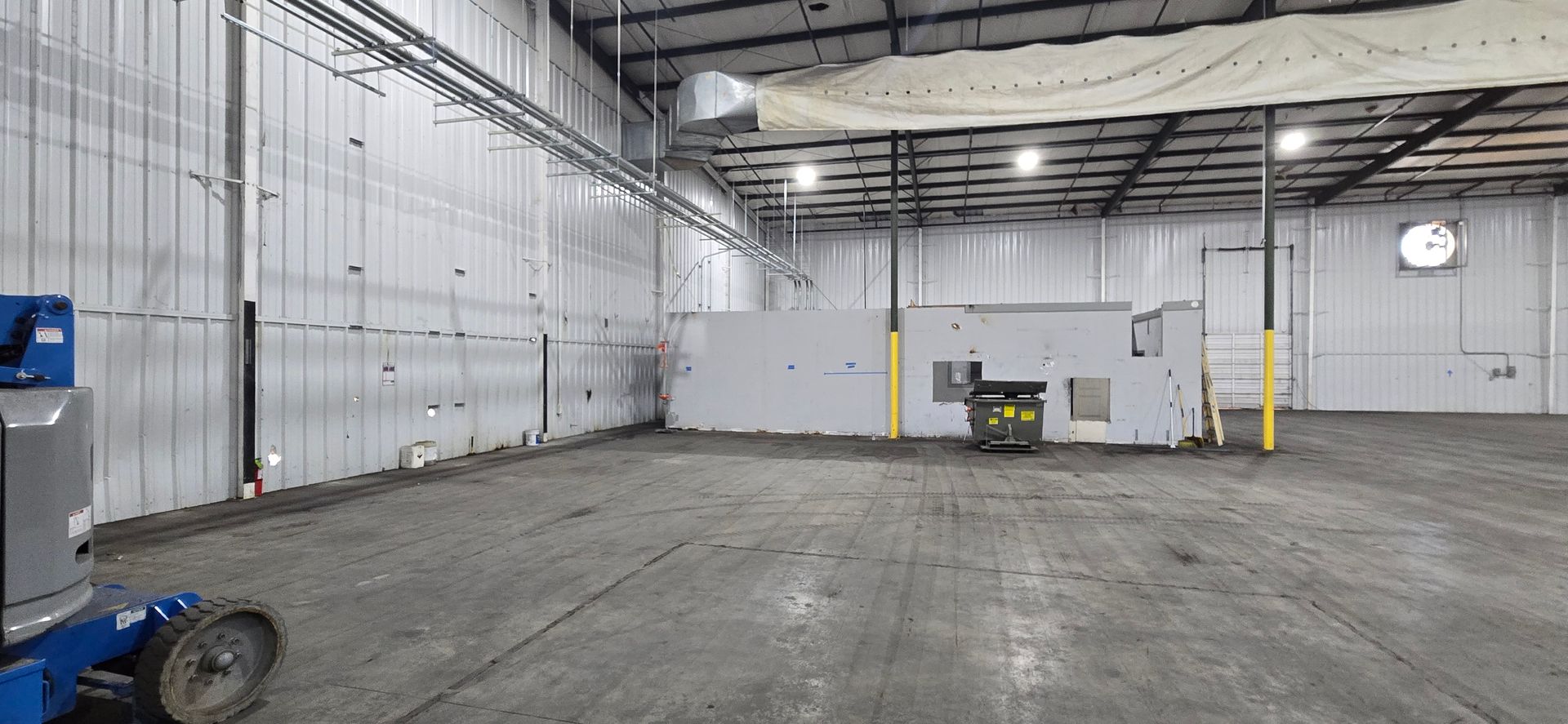 Empty industrial warehouse with concrete floor, white walls, and a forklift near the back wall