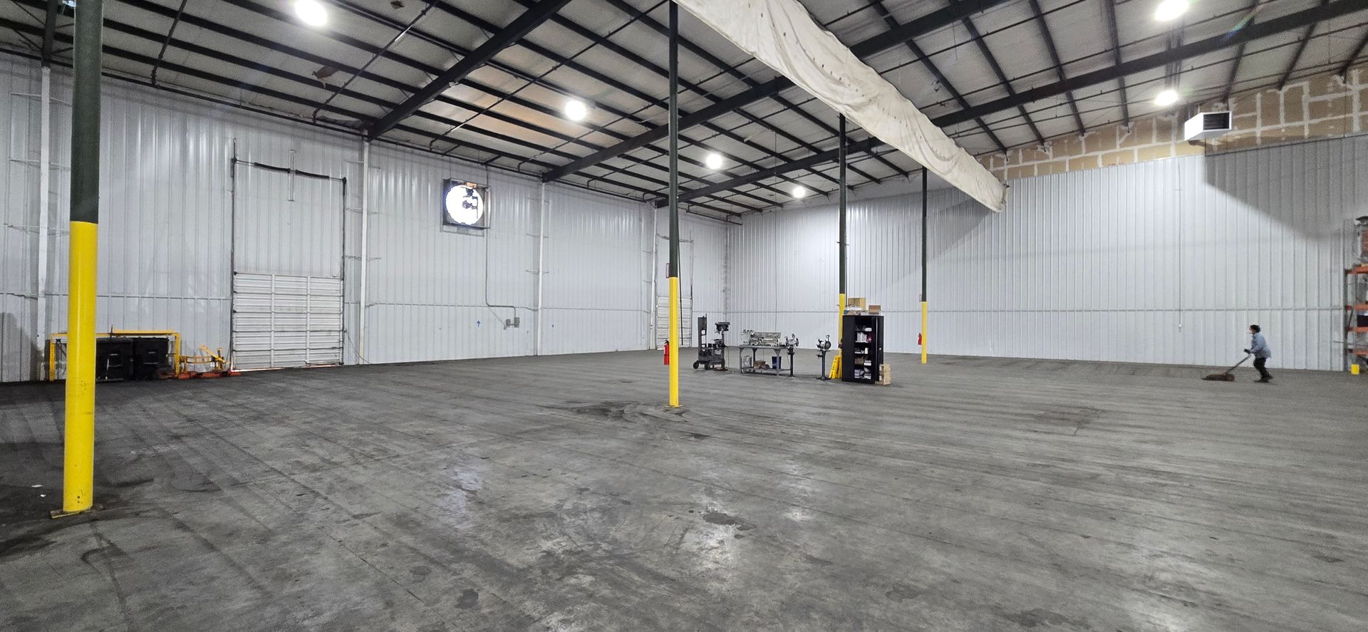 Empty industrial warehouse with concrete floor, white walls, exposed beams, and yellow support columns