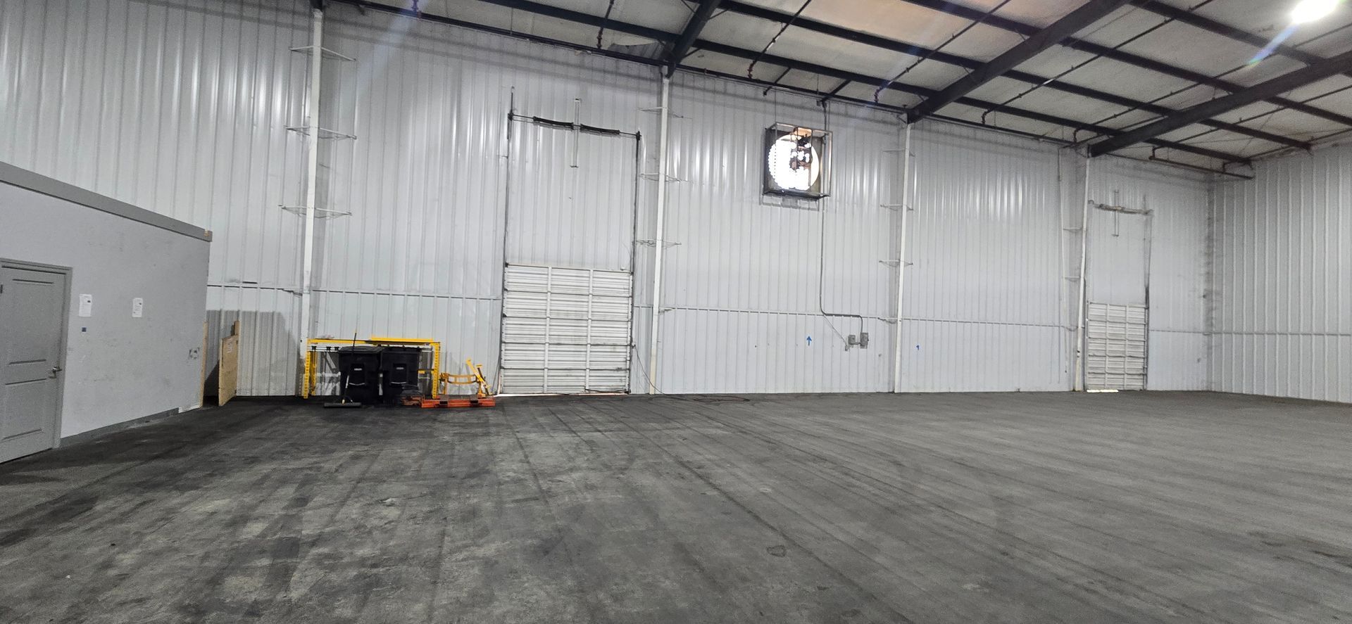 Empty industrial warehouse with concrete floor, white walls, and metal ceiling beams