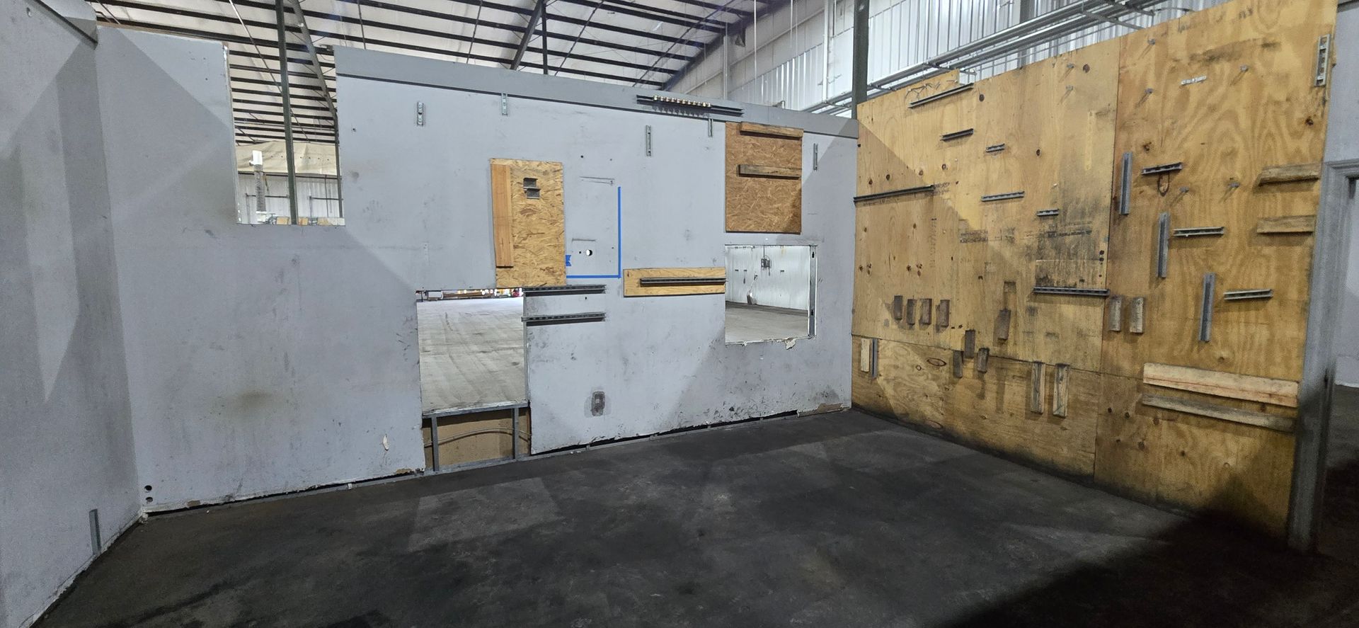 Empty indoor warehouse space with plywood walls, white panels, and a black floor.