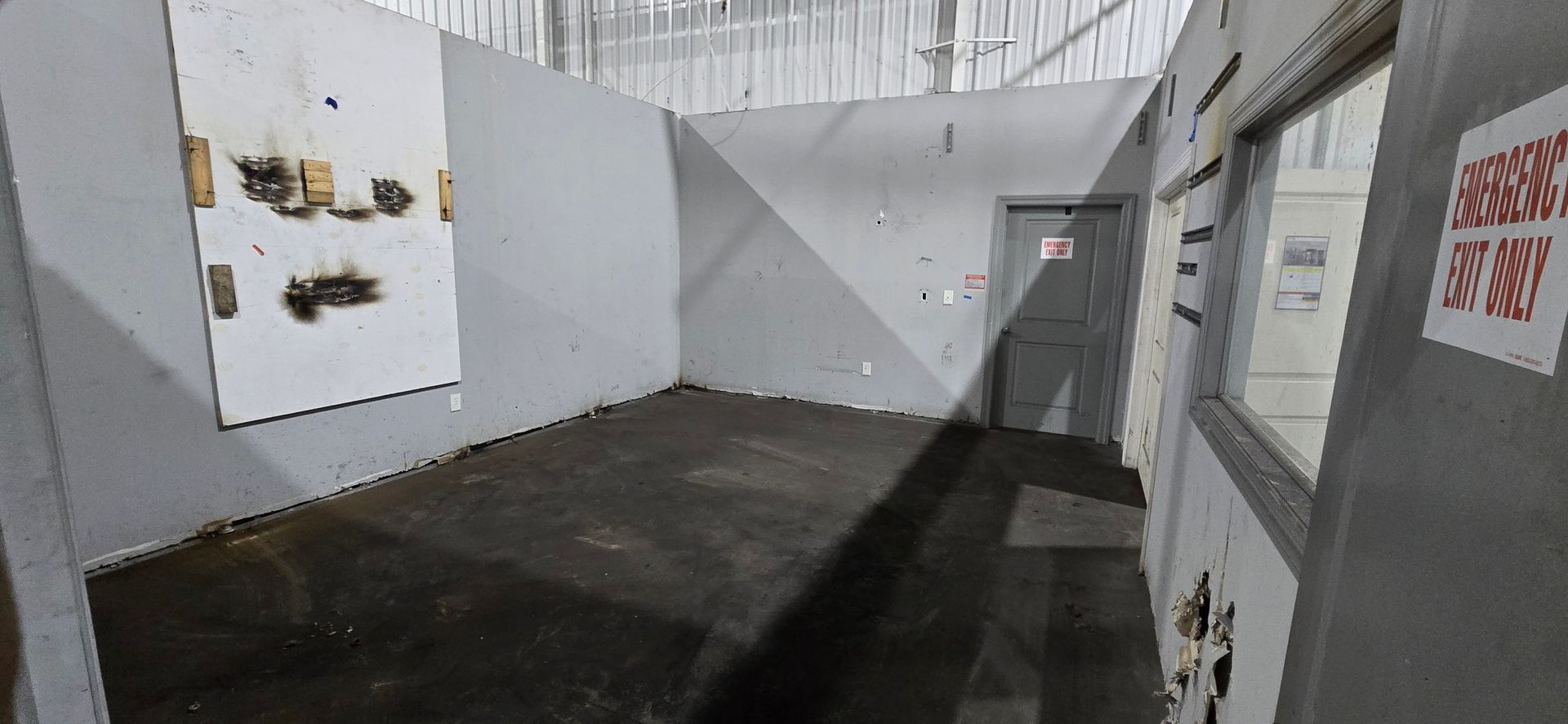 Empty gray hallway with dark floor and white walls, viewed toward a closed door at the end.