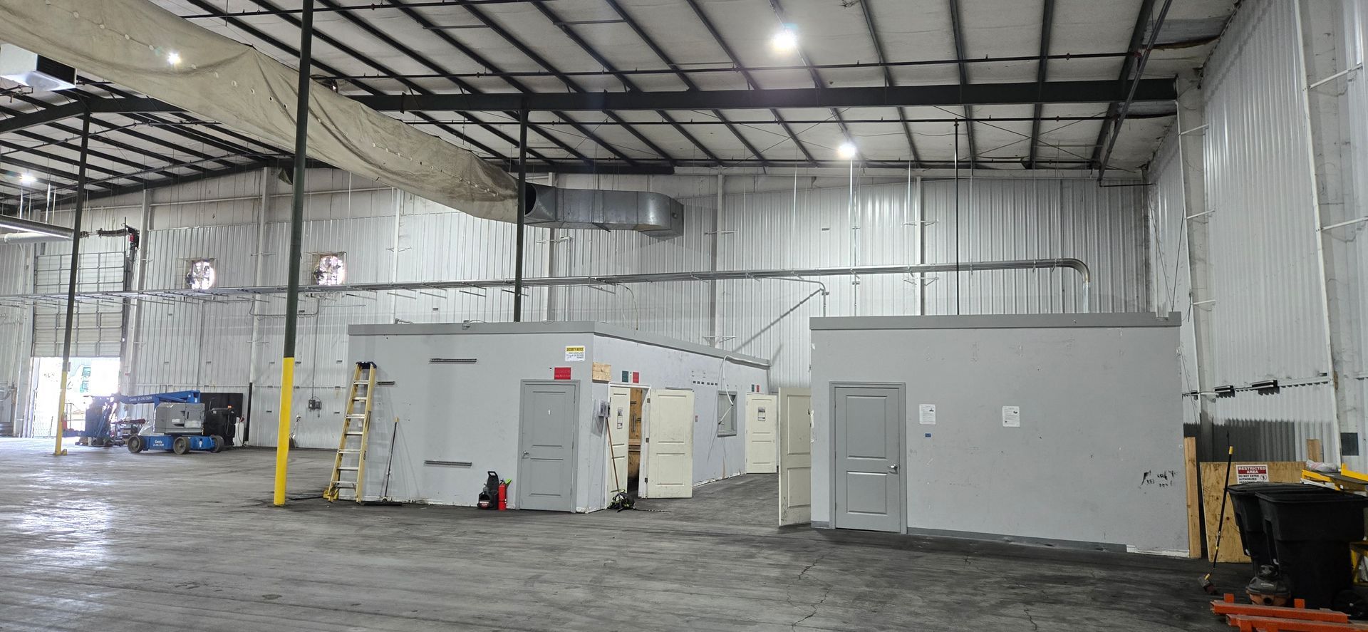 Spacious warehouse interior with white modular office units, concrete floor, and industrial lighting