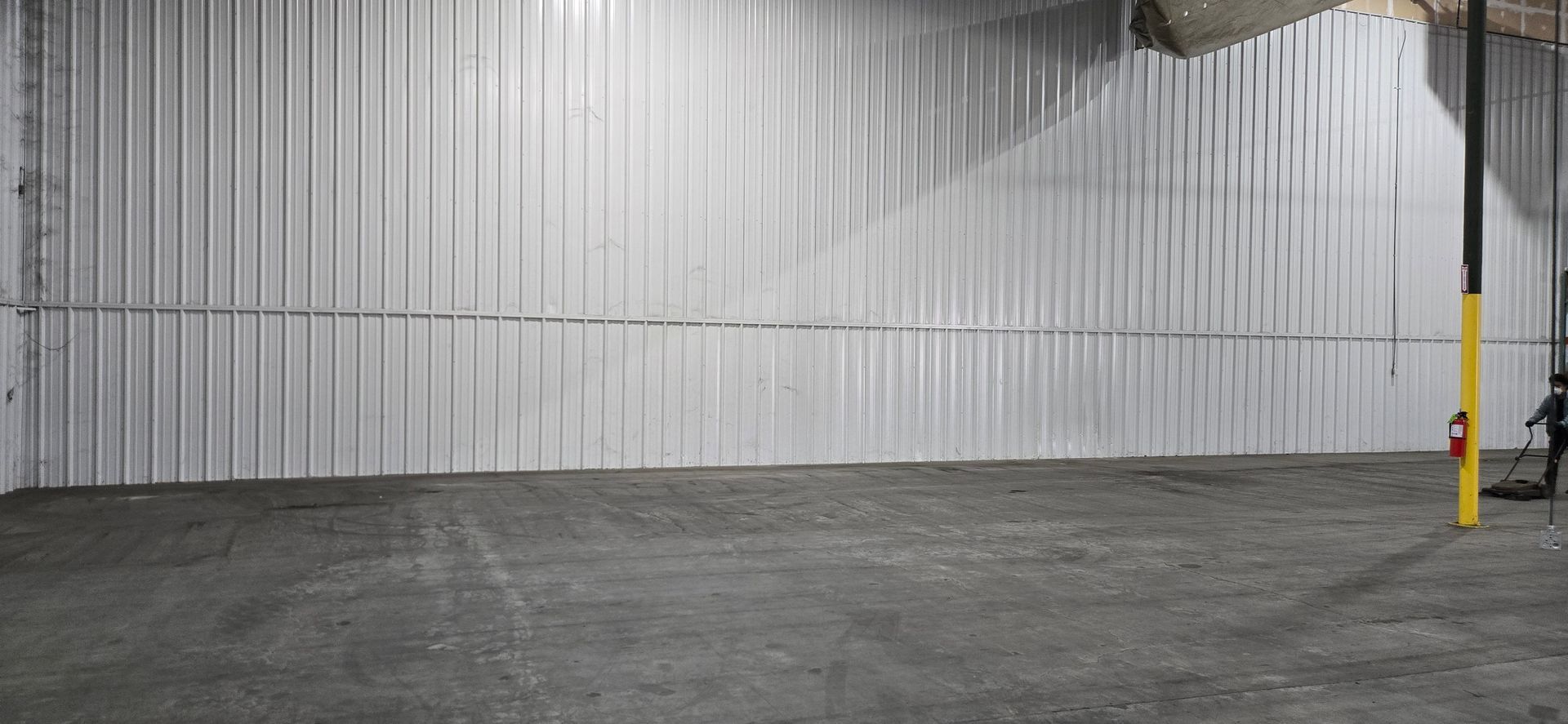 Empty warehouse interior with corrugated metal walls, concrete floor, and a yellow safety post