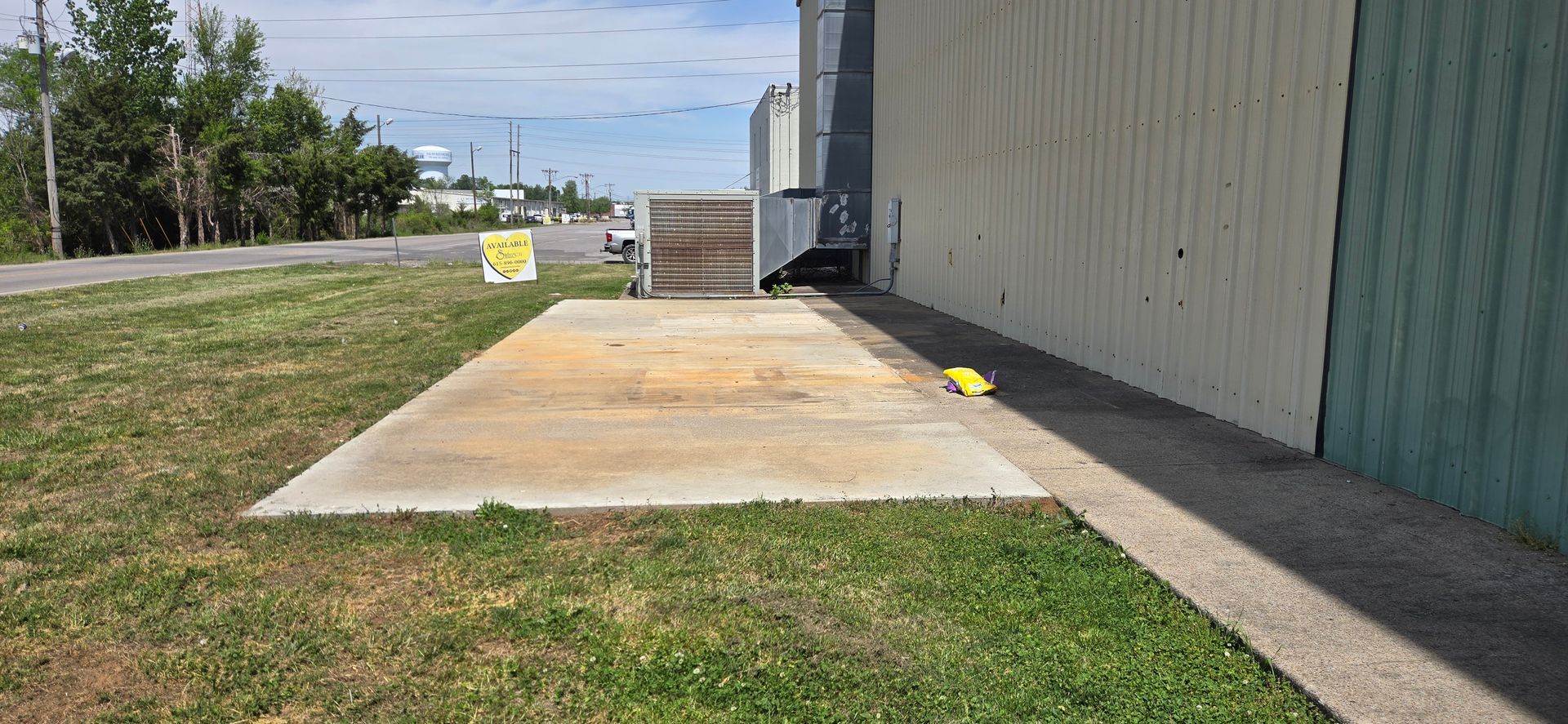 Concrete loading pad beside a metal building, bordered by grass under a clear sky