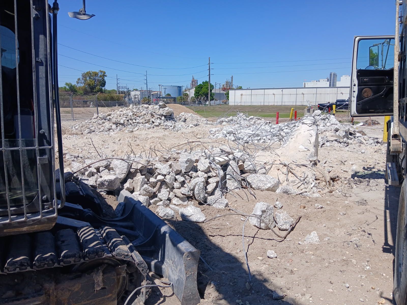 Construction site with rubble pile, excavator tracks, and industrial buildings in the background
