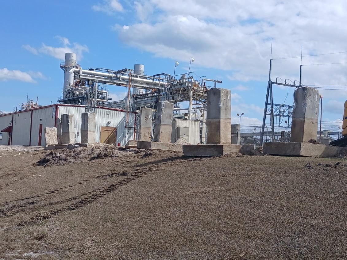 Industrial plant with metal structures, silos, and piping in a barren, muddy landscape under a blue sky
