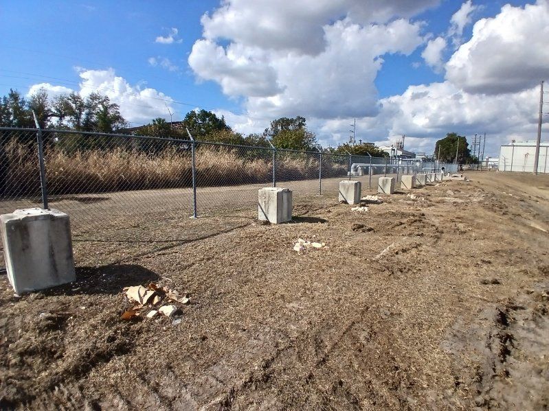 Gravel lot with concrete posts and fencing under a bright, cloudy sky