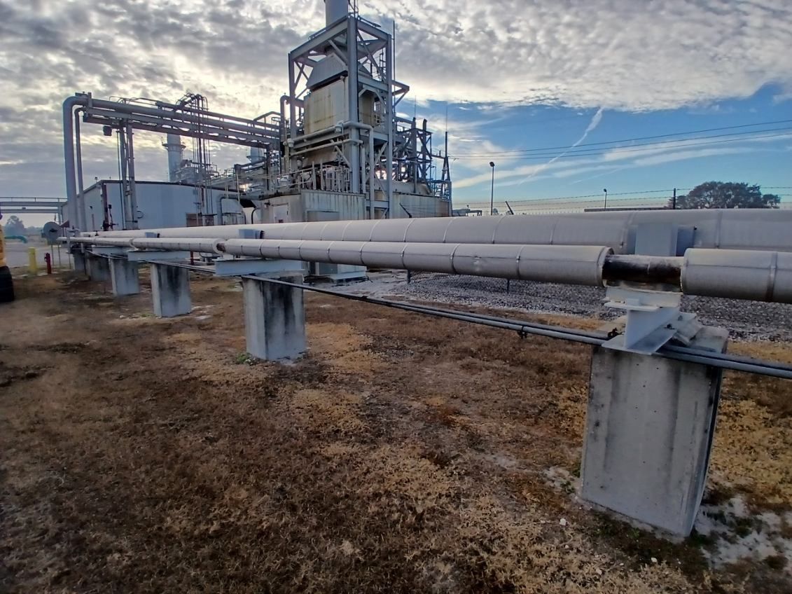 Industrial pipeline and metal framework beside dry grass under a cloudy sky
