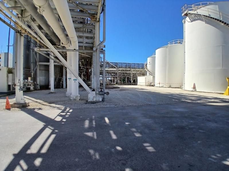 Industrial plant with large white storage tanks, pipes, and a concrete yard under a clear blue sky