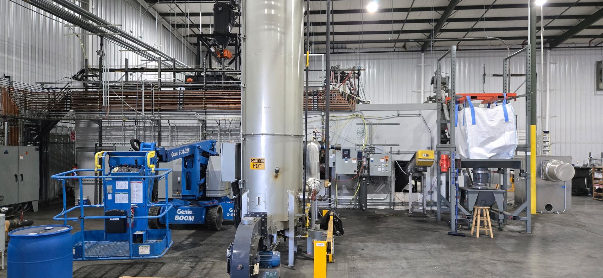 Industrial warehouse interior with blue machinery, metal tanks, and stacked equipment on a concrete floor