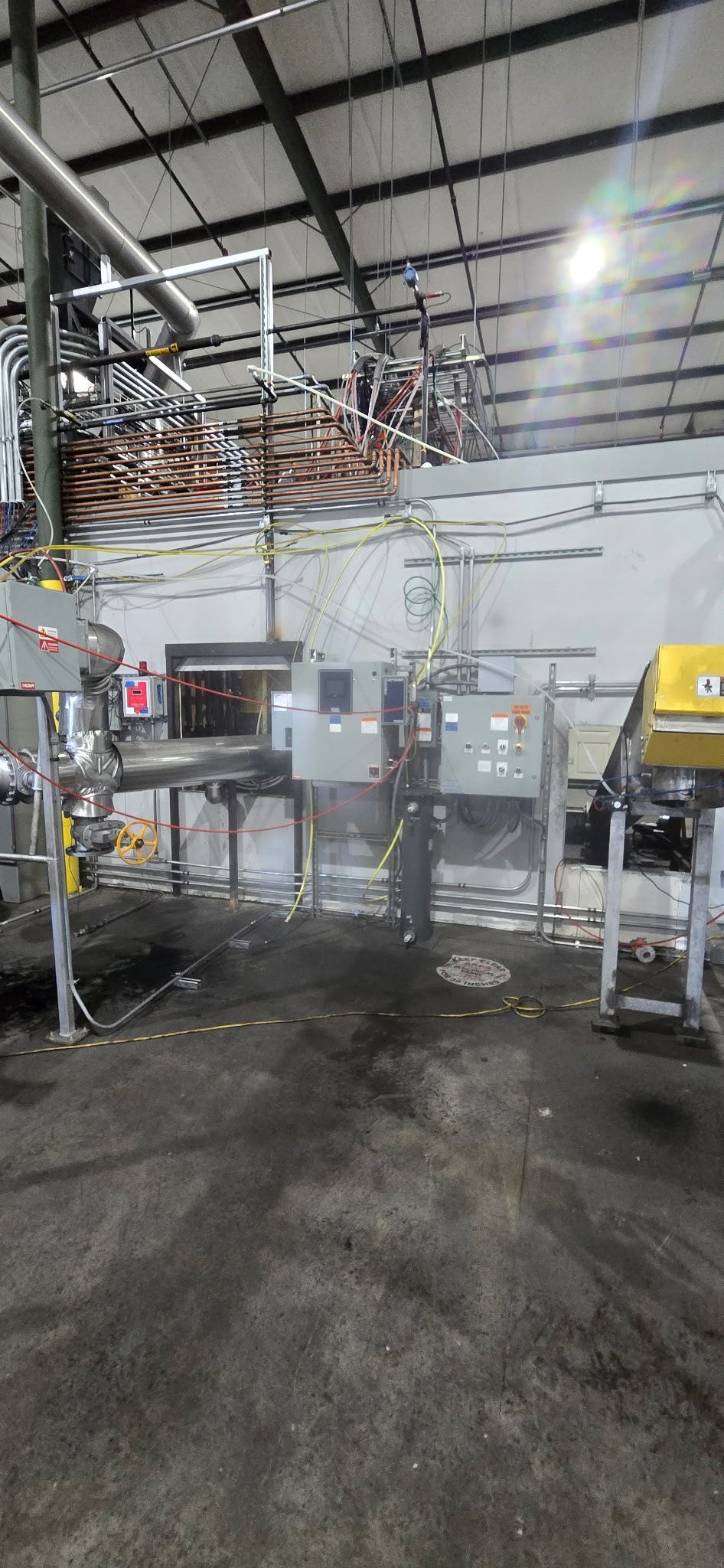 Industrial factory interior with stainless steel processing equipment and overhead piping on a concrete floor