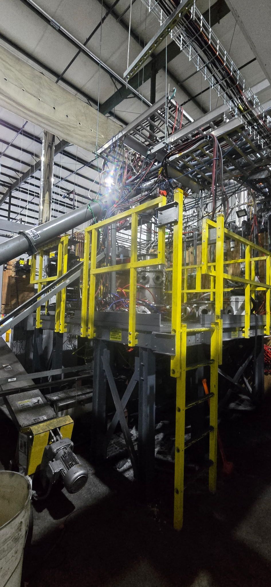 Industrial facility with yellow safety railings around machinery under a high metal ceiling