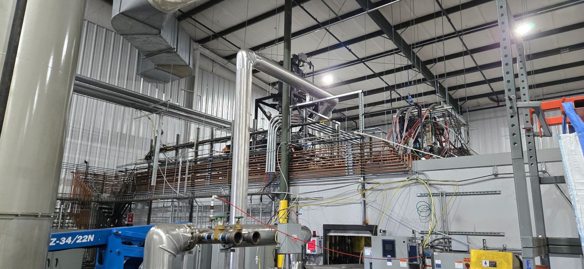 Industrial factory interior with metal piping, machinery, and overhead beams