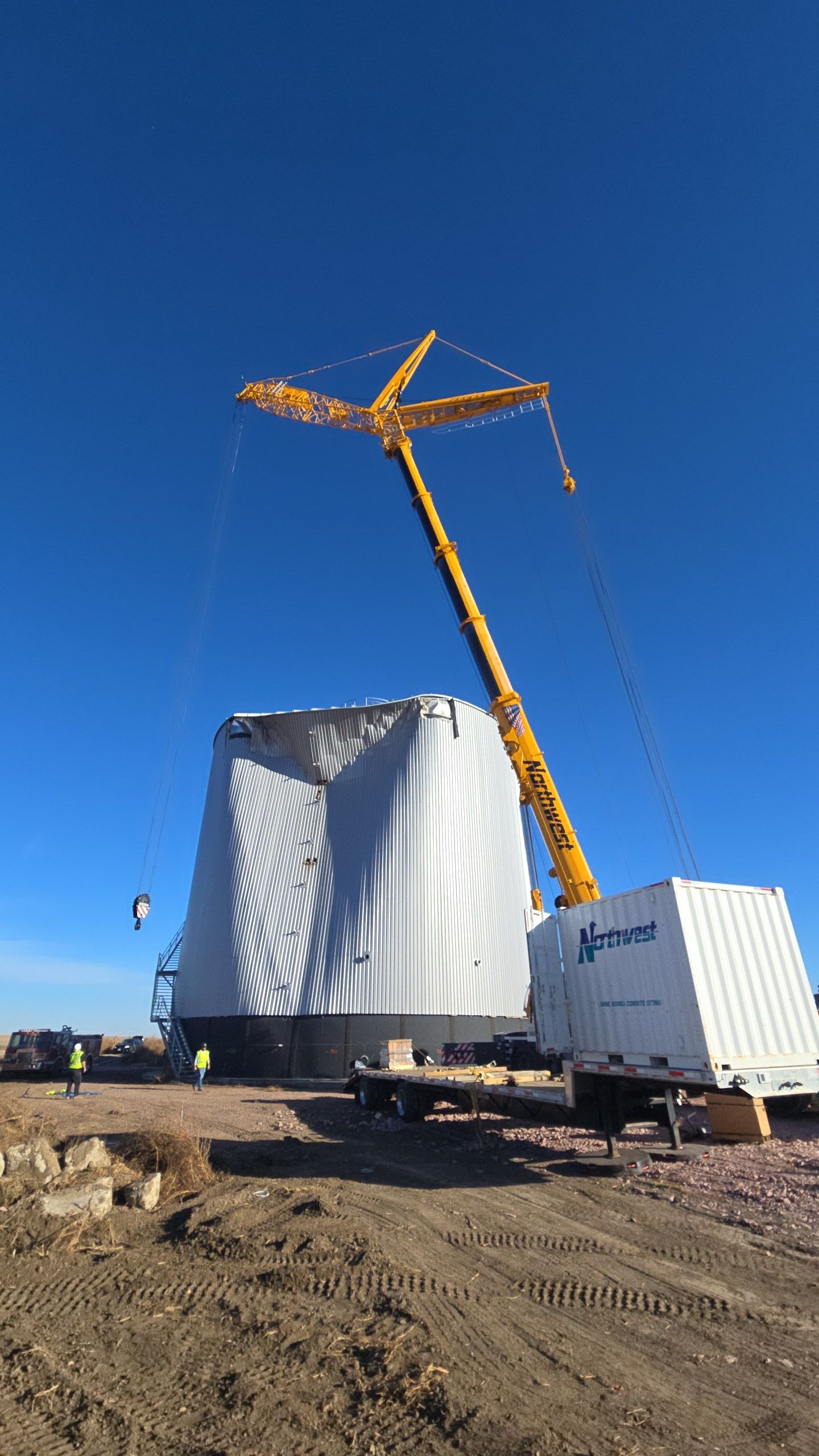 Yellow crane lifting a large white industrial module at a construction site under a clear blue sky