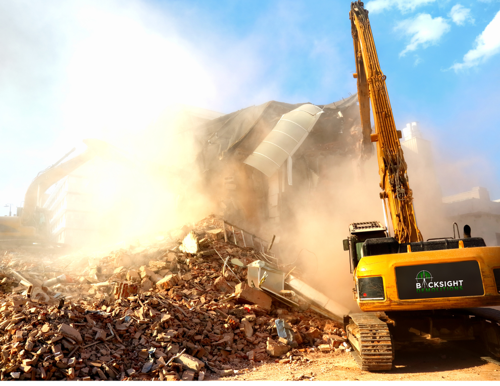A yellow construction excavator demolishes a building, creating a large cloud of dust over a pile of debris.