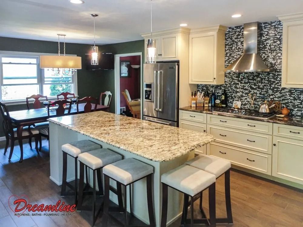 A kitchen with white cabinets , granite counter tops , stools and a refrigerator.