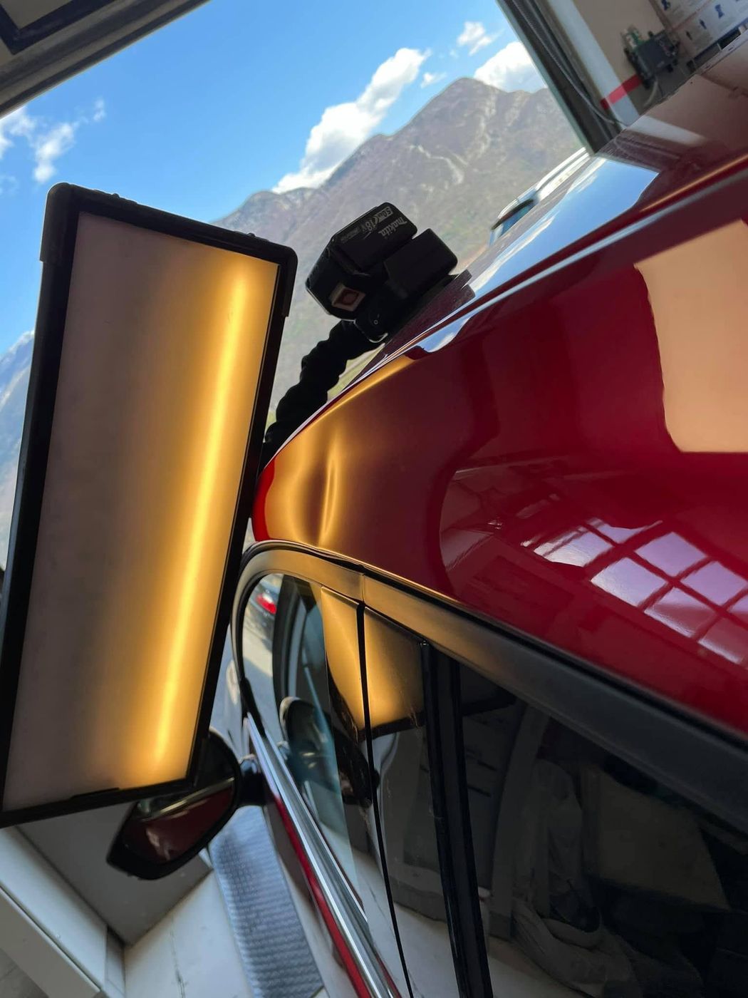 Un'auto rossa viene lucidata con un pannello luminoso accanto e le montagne sullo sfondo.