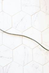 Curved green stem across white hexagonal tile wall with faint gold lines