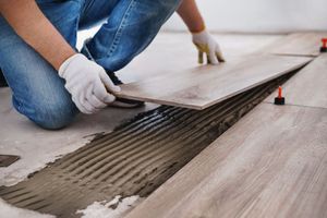 Worker laying wood-look floor tile with adhesive troweled on the subfloor