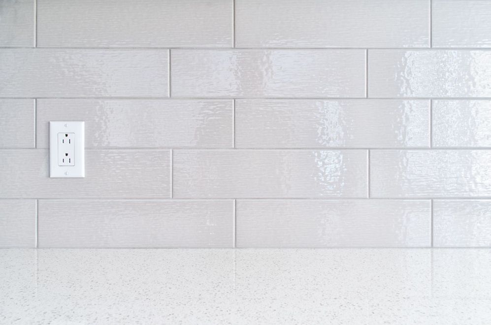 White tiled wall with a wall outlet and light gray countertop edge