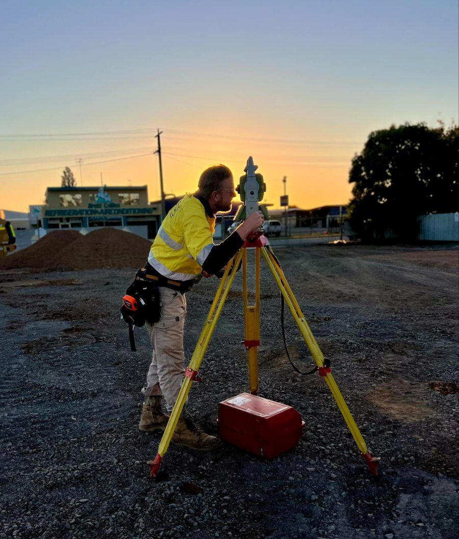 A Man In A Yellow Shirt Is Working On A Tripod At Sunset — Point to Point Surveying In Tatura, VIC