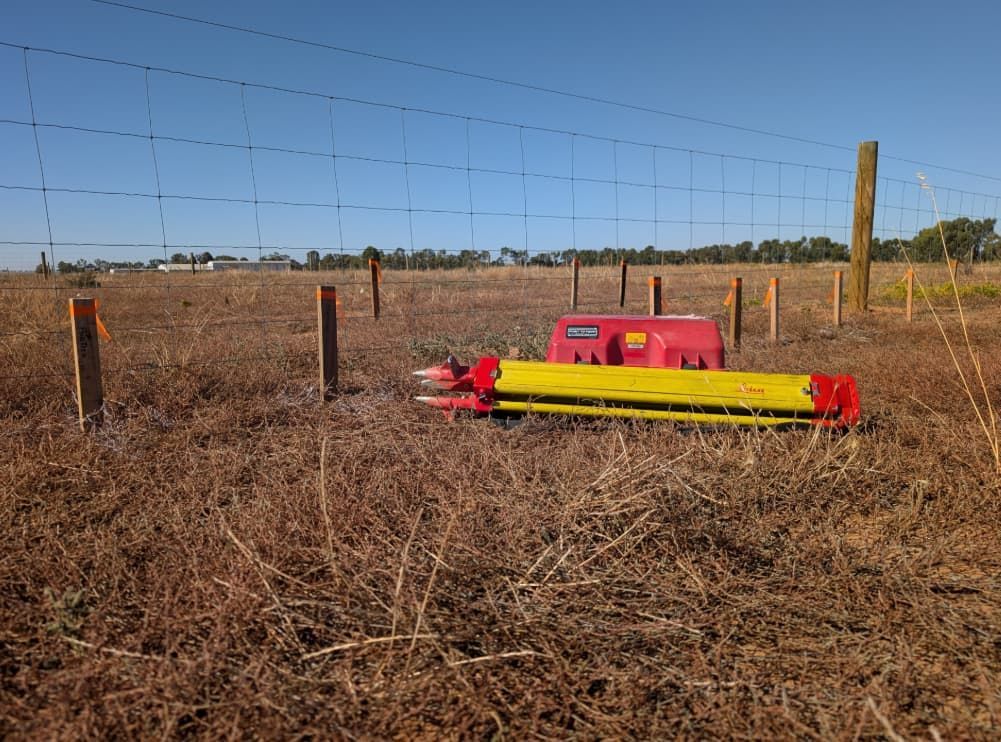 A Red And Yellow Machine Is Sitting In A Field Next To A Barbed Wire Fence — Point to Point Surveying In Kyabram, VIC