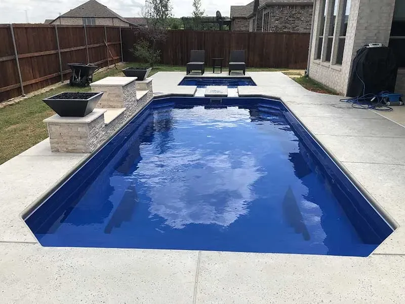 Backyard swimming pool with blue water, white deck, and lounge chairs at the far end