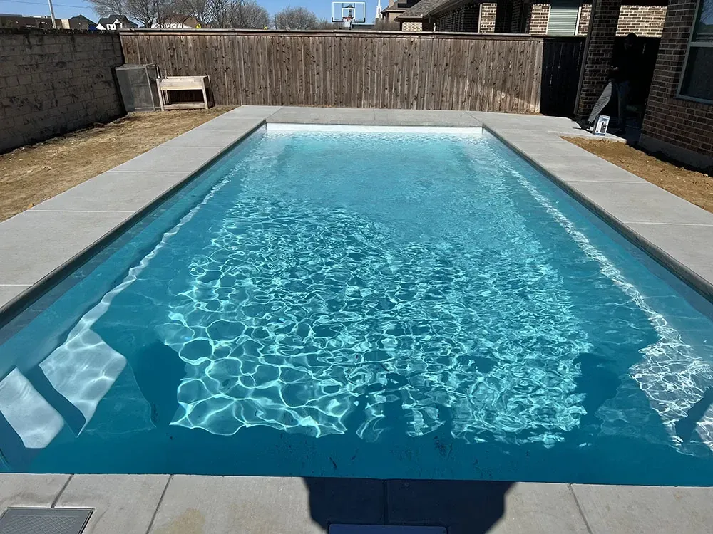 Rectangular backyard swimming pool with clear blue water and stone patio surround