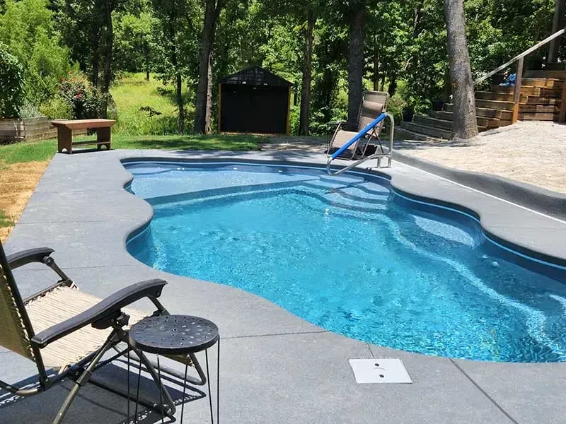 Backyard swimming pool with lounge chairs, diving board, and wooded landscaping