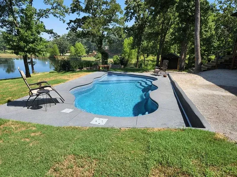 Backyard swimming pool with lounge chairs beside a lake and trees