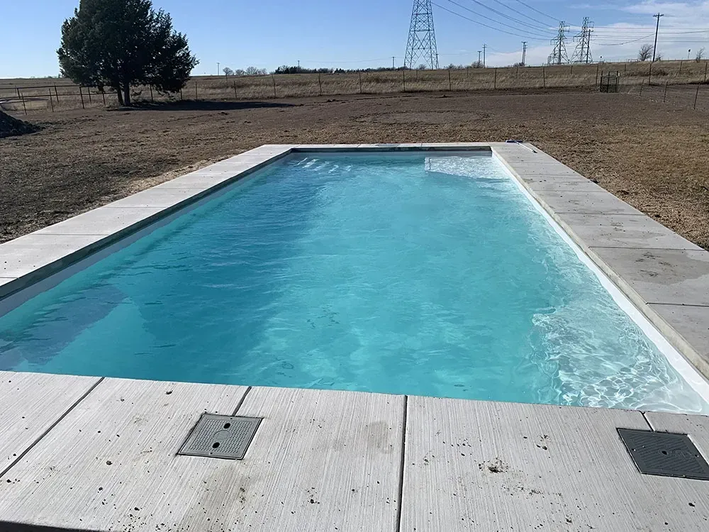 Rectangular outdoor swimming pool with clear blue water in a rural, open landscape