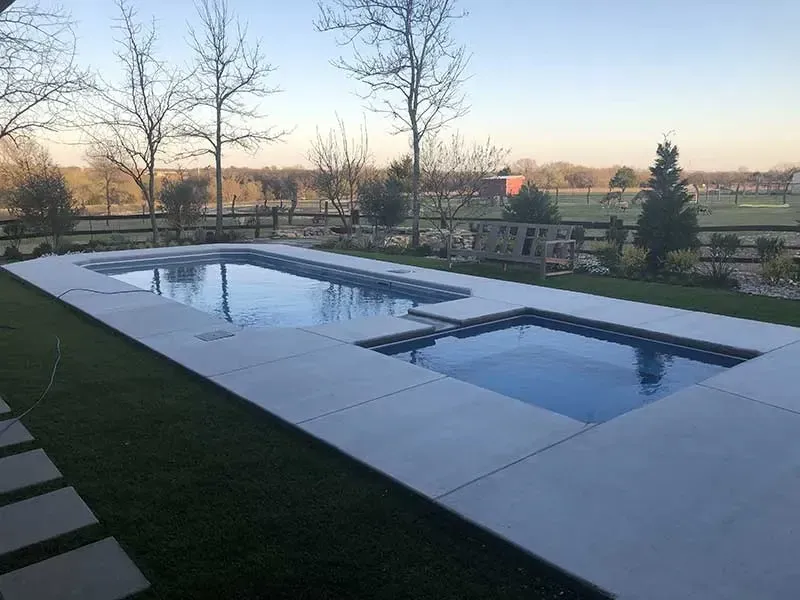Backyard pool with still water, patio, and trees at sunset