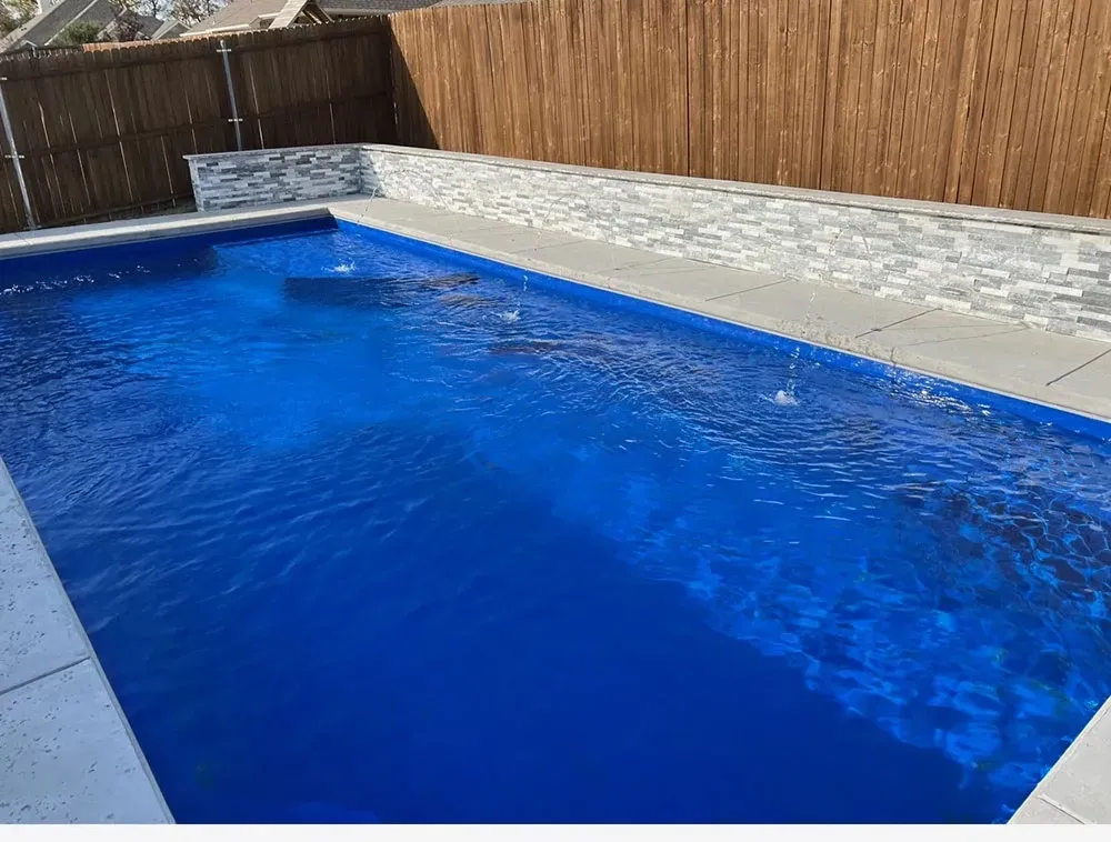 Blue backyard swimming pool beside a stone patio and wooden fence