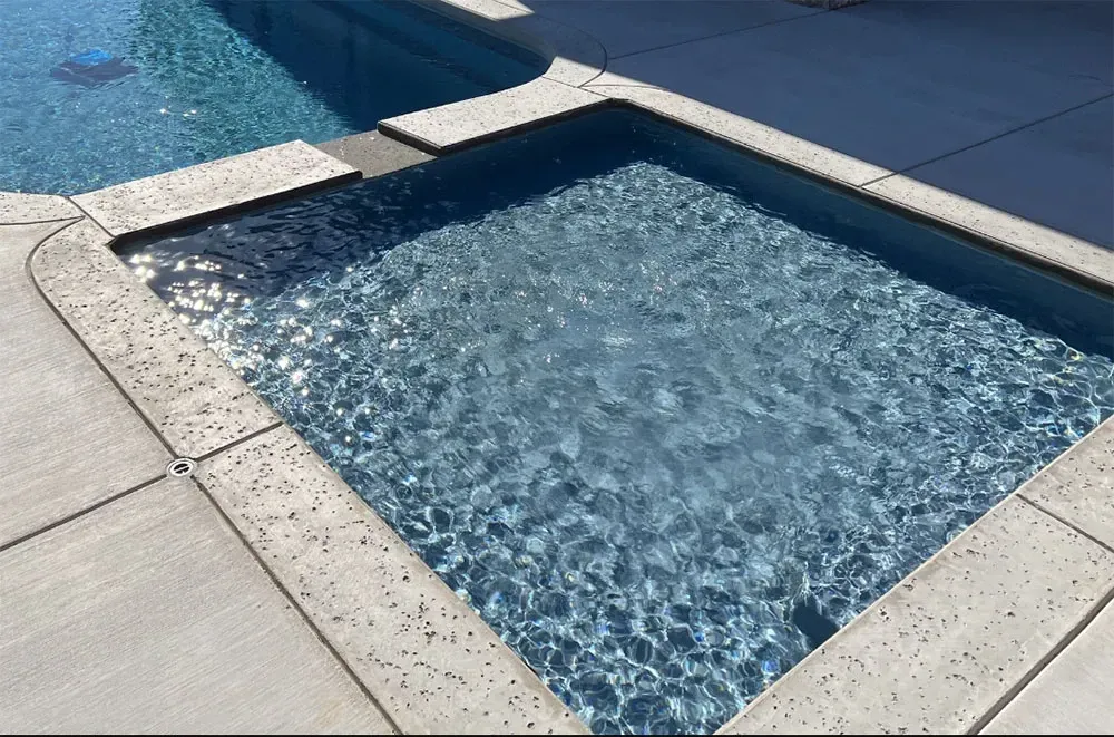 Small square pool of clear blue water beside a concrete deck in bright sunlight