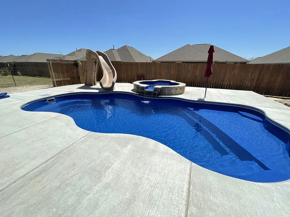 Backyard swimming pool with bright blue water, diving board, and desert homes in the background