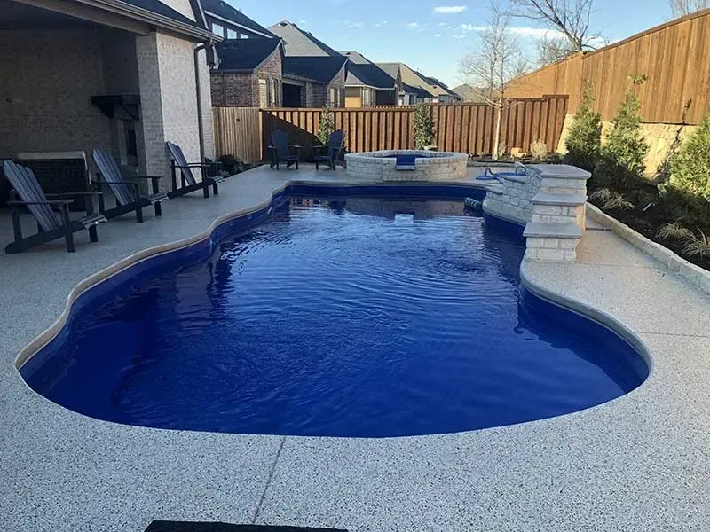Backyard swimming pool with blue water, patio chairs, and a wooden fence