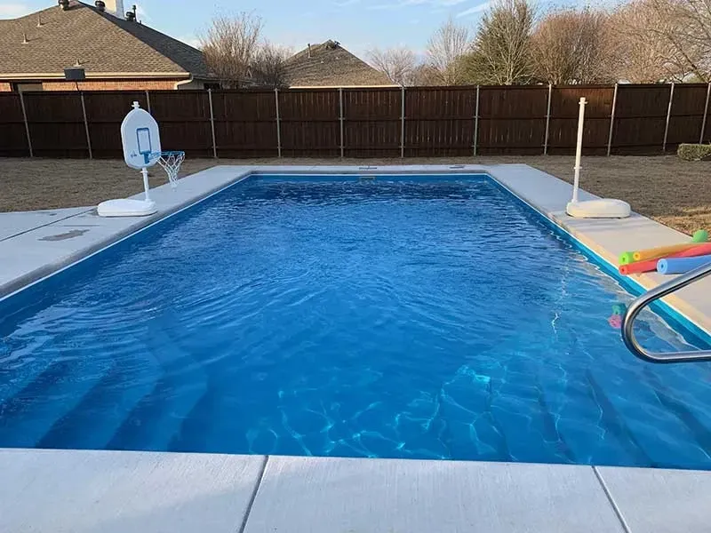 Backyard swimming pool with blue water, diving hoop, and poolside loungers under a clear sky