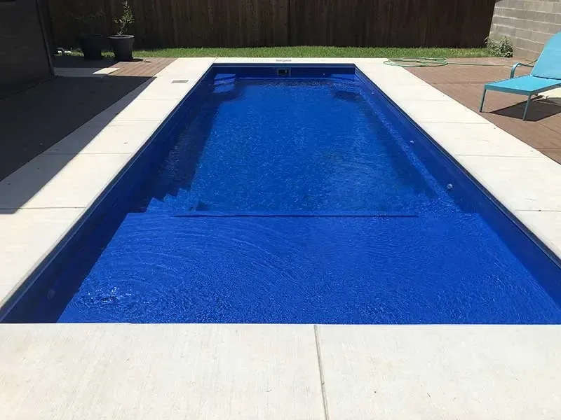Rectangular backyard swimming pool with bright blue water and a light concrete deck