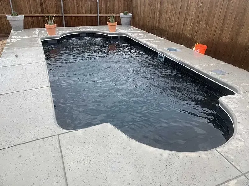 Small outdoor backyard pool with dark water, surrounded by concrete and a wooden fence.