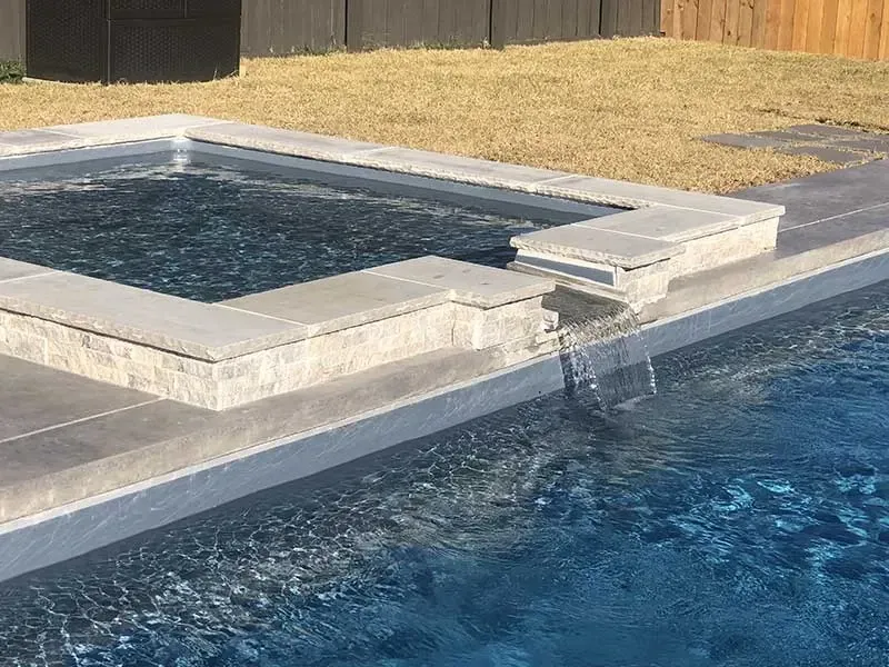 Backyard pool with a raised spa spilling water into the main pool