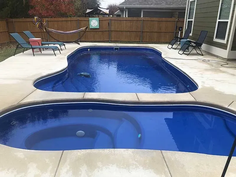 Backyard with two blue swimming pools, patio chairs, and a wooden fence
